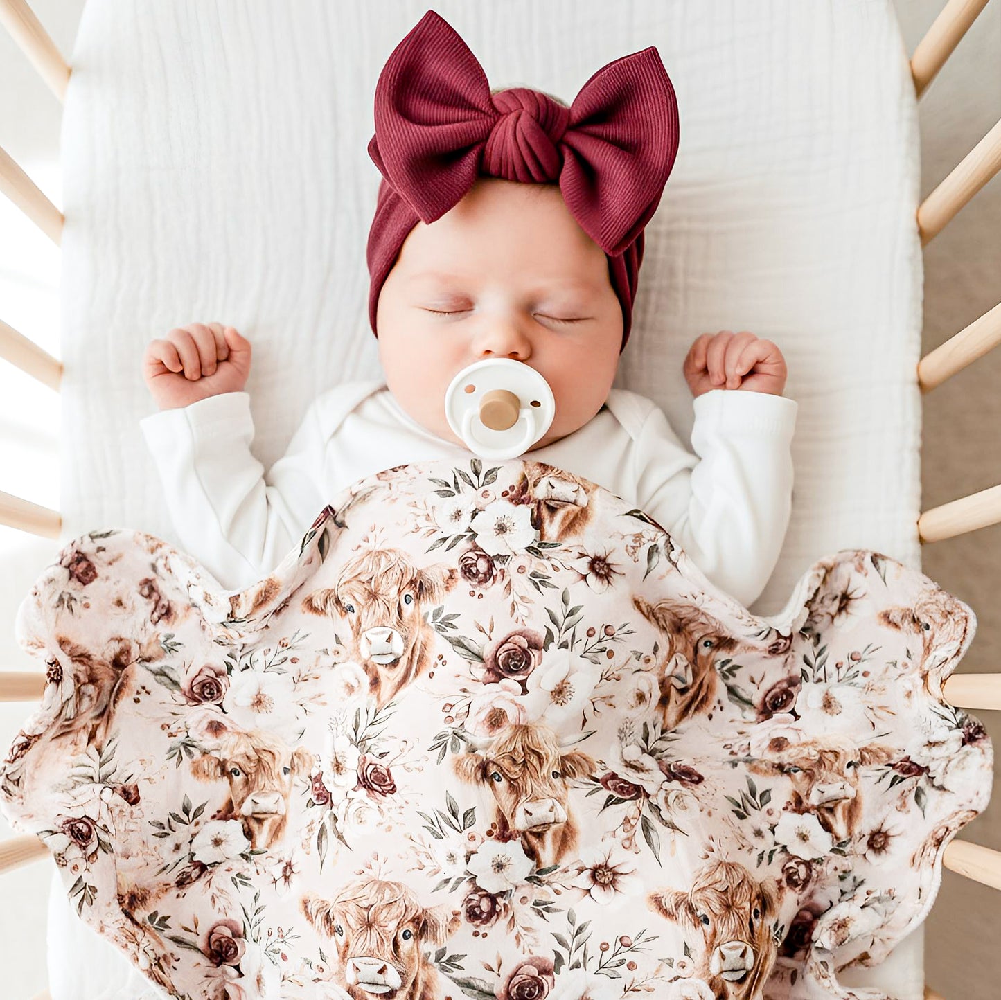 Bébé fille nouveau-né dans une mousseline de bambou vache highland sur le thème des fleurs et de la ferme country, fait au Québec, Canada, ave cune suce Bibs dans la bouche et un bandeau bourgogne avec une boucle, le bébé dort d'un sommeil profond