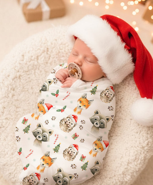 Bébé dormant dans une couverture de Noël avec motifs d’animaux, portant un bonnet du Père Noël, ambiance chaleureuse et festive.