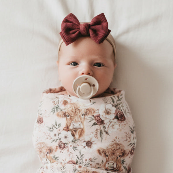 Bébé fille nouveau-né dans une mousseline de bambou vache highland sur le thème des fleurs et de la ferme country, fait au Québec, Canada, ave cune suce Bibs dans la bouche et un bandeau bourgogne avec une boucle